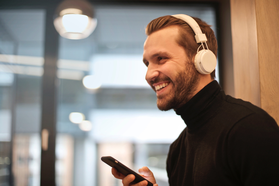Smiling man wearing white over-ear headphones in a bright modern setting, evoking healthy hearing and gentle ear care