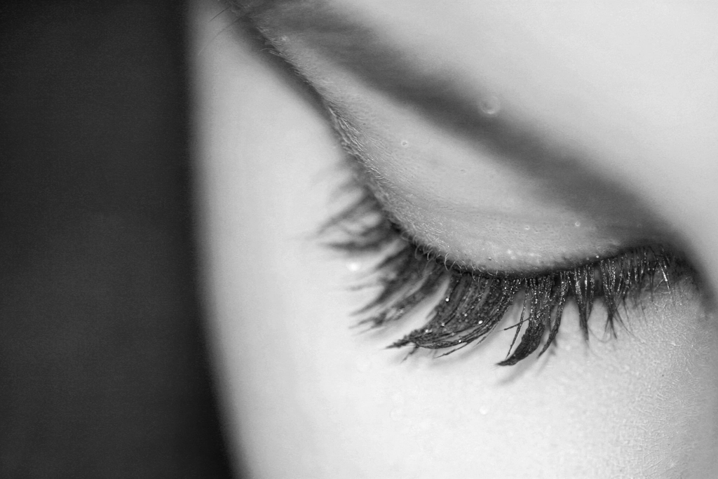 Tasteful black-and-white beauty close-up of a woman's closed eye showing long, full, well-defined natural eyelashes