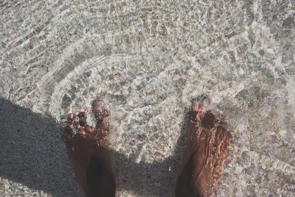 Healthy bare feet standing in crystal-clear shallow water over a clean pebbled seabed, evoking clean, well-cared-for nails and foot care