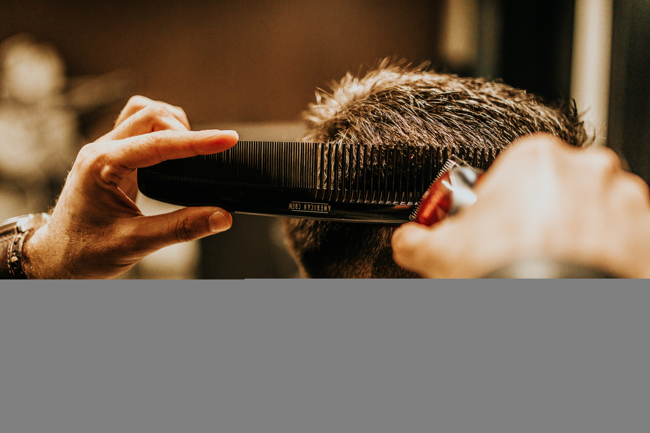 A barber combing and grooming a man's thick, healthy hair in a warm, professional barbershop