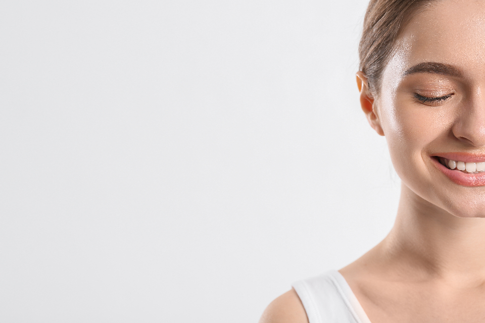 Smiling young woman with smooth, clear, radiant skin against a soft light background, with open space to the left for headline text