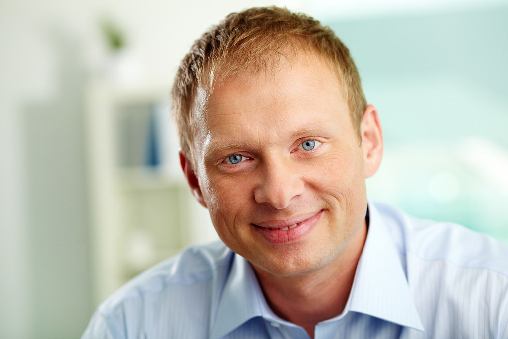 A confident, healthy man smiling warmly in a bright, softly blurred wellness setting