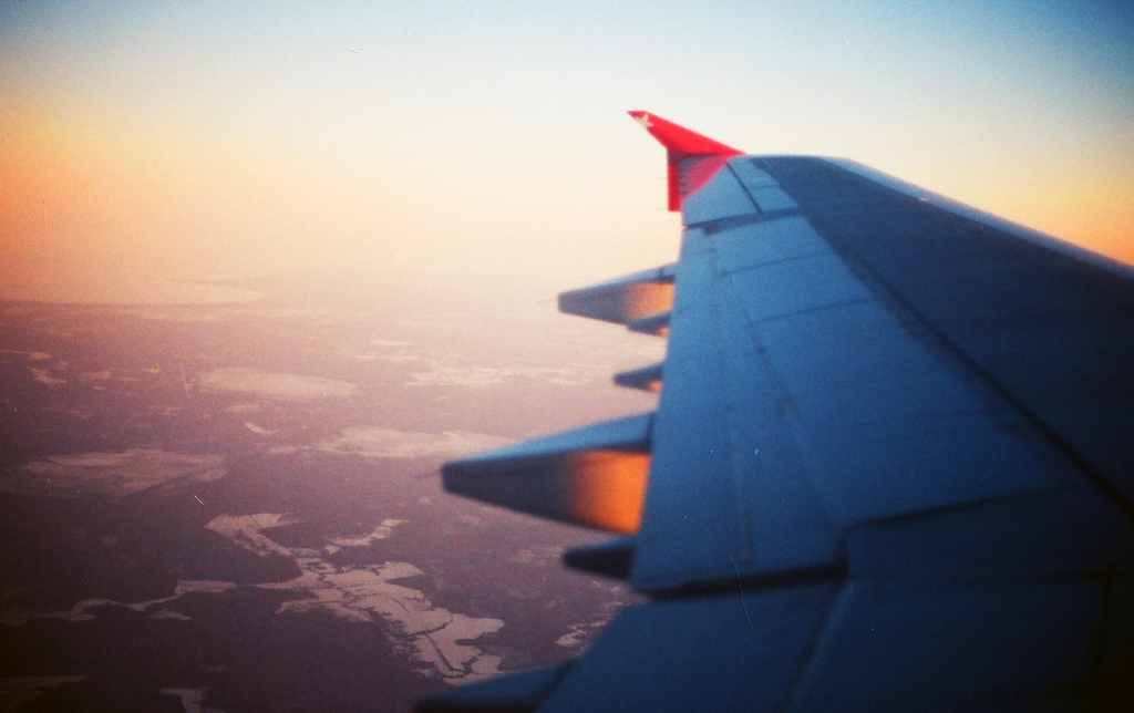 Warm golden-hour view from an airplane window, looking out over the wing across the landscape far below — evoking long-haul air travel and jet lag.