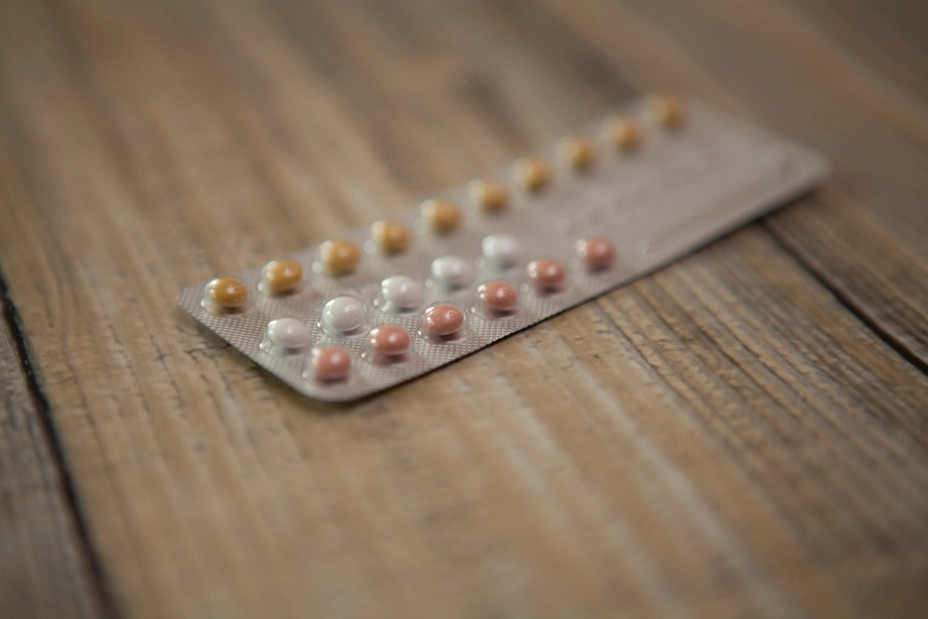 A contraceptive pill blister pack resting on a warm wooden surface, softly lit with shallow depth of field
