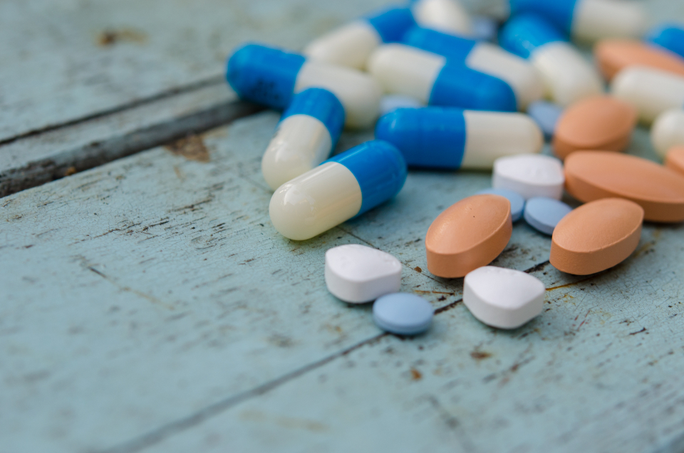 An assortment of tablets and capsules arranged on a soft pale-wood surface, a calm and discreet image representing pharmacy medication.